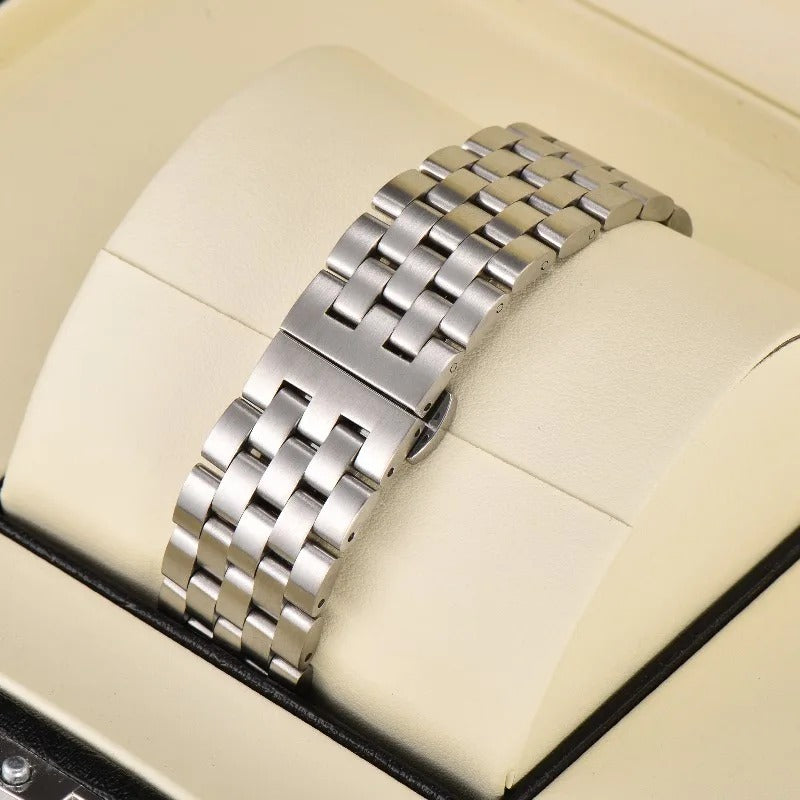 Brushed silver-toned metal watch bracelet with a multi-link design and deployant clasp displayed on a cream padded cushion inside a black watch box